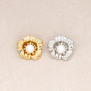 May include: Two flower-shaped pins, one in a polished gold tone and one in a polished silver tone. Each pin features five rounded petals with a textured, grooved surface and a single, smooth, round white pearl set in the center of the flower.