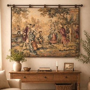 Op de afbeelding: Een groot wandtapijt met een historische scène met figuren in historische kleding, hangend boven een houten console. De tafel heeft laden, een onderste plank en decoratieve items zoals een vaas, kom en kandelaar.