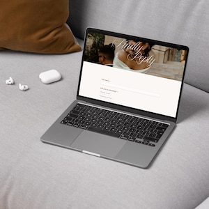 May include: A dark gray laptop displaying a digital wedding RSVP form on its screen. The webpage features the text Kindly Reply, a field for Full Name, and a dropdown menu for attendance status. Two white wireless earbuds are placed next to the laptop.