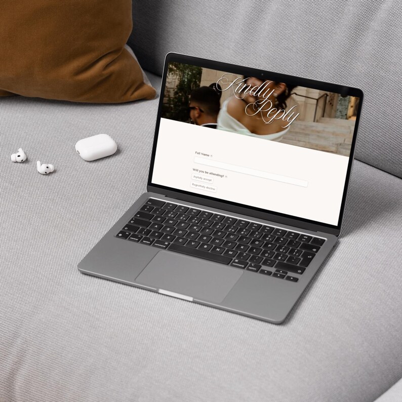 May include: A dark gray laptop displaying a digital wedding RSVP form on its screen. The webpage features the text Kindly Reply, a field for Full Name, and a dropdown menu for attendance status. Two white wireless earbuds are placed next to the laptop.