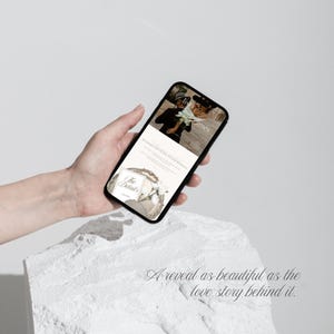 May include: A black smartphone displaying a digital wedding invitation on its screen. The screen shows the text Livia & James, The Details, and a floral graphic. The interface features a soft color palette with white and beige tones throughout.