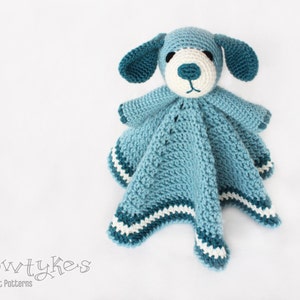 May include: A blue crocheted dog-shaped baby blanket with white accents. The blanket has a crocheted face with white eyes and a nose.