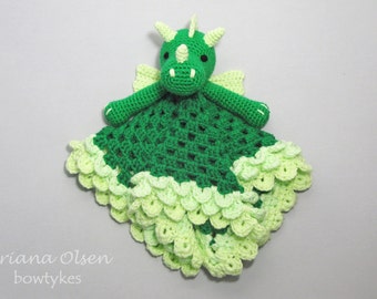 Op de afbeelding: Groene gehaakte babydeken met een draakmotief en een lichtgroene geruite rand. De draak heeft een groen lichaam, lichtgroene vleugels en zwarte ogen.