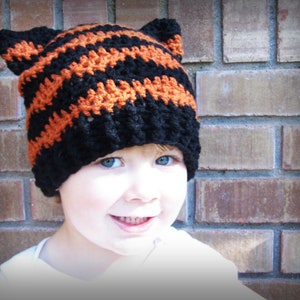 May include: A child wearing a black and orange striped crocheted hat with cat ears.