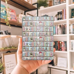 May include: A clear phone case featuring a colorful, whimsical design of bookshelves filled with books, plants, and mushrooms. The design is in pastel colors, with a repeating pattern of the bookshelf motif.
