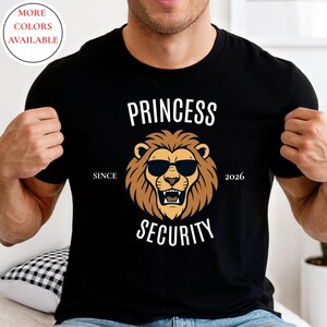 Może przedstawiać: Czarna koszulka z grafiką lwa w okularach przeciwsłonecznych. Tekst brzmi "PRINCESS SECURITY" z "SINCE 2026" nad i pod wizerunkiem lwa. Okrąg w lewym górnym rogu mówi "MORE COLORS AVAILABLE".