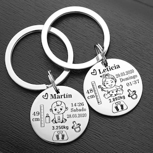 May include: Two silver keychains with engraved baby details. One keychain says "Martín" with baby stats: 49 cm, 3.250kg, and the date and time. The other says "Leticia" with stats: 48 cm, 2.892kg, and the date and time.