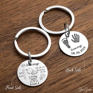 May include: Two silver keychains with engraved round charms. One charm displays baby footprints and a handprint, with the name "Александр" and date 08.26.2019. The other charm shows baby details: 49 cm, 2.850kg, and the date and time.