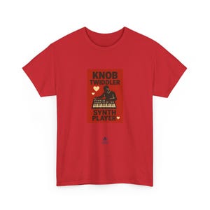 Può includere: T-shirt rossa con grafica rettangolare. La grafica presenta le parole "KNOB TWIDDLER" e "SYNTH PLAYER", una silhouette di una persona che suona un sintetizzatore e due cuori.