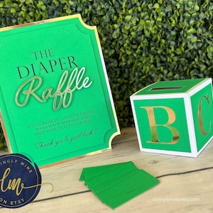 May include: Green and gold diaper raffle sign with a white and green box with gold letters that spell "BC". The sign says "The Diaper Raffle" and "If you brought a pack of diapers please place them here and drop your ticket in the box. Thank you & good luck!"