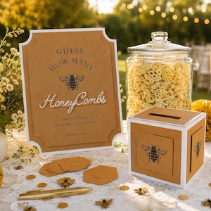 May include: A tan sign with black text reading GUESS HOW MANY HoneyCombs ARE IN THE JAR, THE CLOSEST GUESS WINS! GOOD LUCK, featuring a bee illustration. Next to it is a clear glass jar filled with honeycomb cereal and a tan square ballot box.