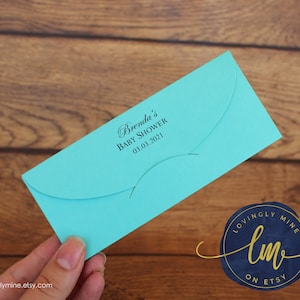 May include: A bright turquoise rectangular envelope with a curved flap. The front is printed with black text that reads Brenda's Baby Shower and the date 03.03.2021 in a combination of script and sans-serif fonts, featuring a secure closure slot.