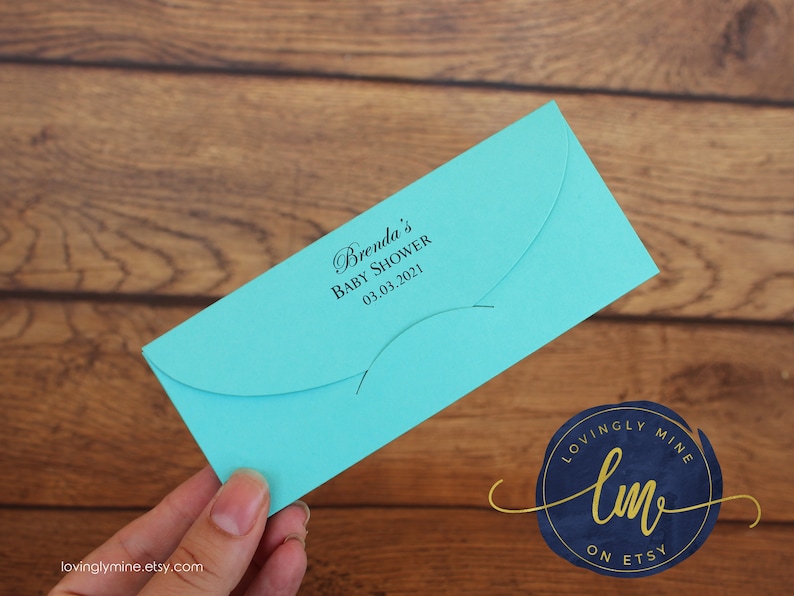 May include: A bright turquoise rectangular envelope with a curved flap. The front is printed with black text that reads Brenda's Baby Shower and the date 03.03.2021 in a combination of script and sans-serif fonts, featuring a secure closure slot.