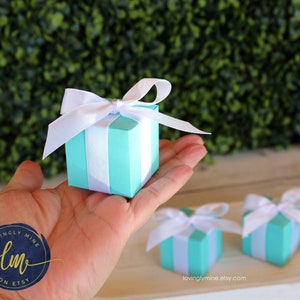 May include: Three small turquoise blue gift boxes with white ribbon bows. The boxes are striped with white and turquoise blue. The boxes are on a white surface with a green background.