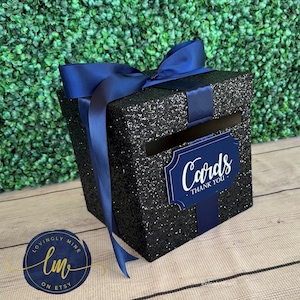 May include: Black glitter card box with a navy blue ribbon and a sign that says "Cards - Thank You".