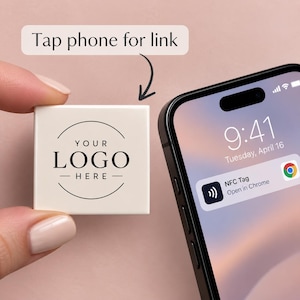 May include: A square white NFC tag featuring the black text YOUR LOGO HERE inside a circular frame. A smartphone is positioned nearby displaying a notification that reads NFC Tag Open in Chrome. Text above the tag reads Tap phone for link.