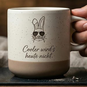 Könnte beinhalten: Eine weiße Keramik-Tasse mit schwarzem Henkel und dem Text "But First, Coffee" in schwarzer, fetter Schrift. Die Tasse steht auf einer weißen Oberfläche.
