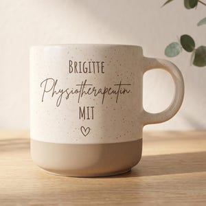 Könnte beinhalten: Ein zweifarbiger Keramikbecher mit einem gesprenkelten cremefarbenen oberen Teil und einem beigen Boden. Der Text "BRIGITTE Physiotherapeutin MIT" ist in Schwarz aufgedruckt, gefolgt von einem kleinen, handgezeichneten Herzsymbol unter dem Text.