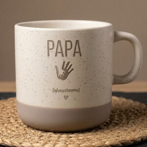 Pode incluir: Um conjunto de três canecas de cerâmica com acabamento fosco e salpicado. As canecas são em tons de creme, cinza claro e cinza escuro. Cada caneca tem um design simples e moderno e uma alça arredondada.