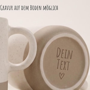 May include: Two ceramic mugs with a speckled off-white glaze and a solid beige base. The bottom of one mug features the engraved text DEIN TEXT and a small heart symbol. The text GRAVUR AUF DEM BODEN M&Ouml;GLICH is visible at the top of the image.