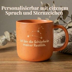 Könnte beinhalten: Ein Set aus drei Keramikbechern mit gesprenkelter, matter Oberfläche. Die Becher sind in Creme-, Hellgrau- und Dunkelgrautönen gehalten. Jeder Becher hat ein schlichtes, minimalistisches Design und einen abgerundeten Griff.