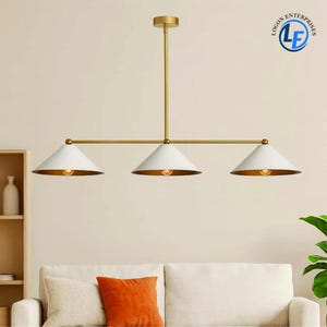Peut inclure: Une suspension moderne à trois lumières avec une finition dorée et des abat-jours blancs en forme de cône. L'intérieur de chaque abat-jour est doré et contient une ampoule. La lampe est suspendue au plafond par une tige dorée.