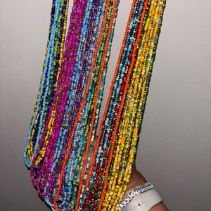 May include: A selection of colourful beaded strands in shades of blue, pink, orange, and green. The small beads are strung together, creating a textured effect. The strands are held together, displaying the vibrant colours and patterns.