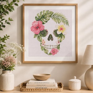 May include: A framed cross-stitch artwork featuring a skull shape composed of various tropical leaves and vibrant flowers, including pink hibiscus and white plumeria, set against a light pink grid background within a light wood frame.