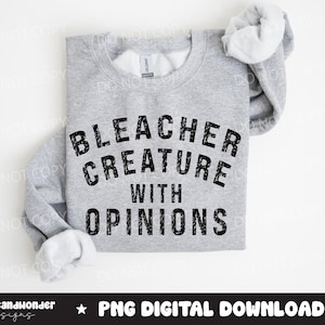 May include: A light gray sweatshirt with the text "BLEACHER CREATURE WITH OPINIONS" in black, distressed font. The sleeves are folded over. The bottom of the image has the text "graceandwonder designs" and "PNG DIGITAL DOWNLOAD".