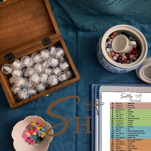 Peut inclure: Une boîte en bois remplie de récipients en plastique transparent avec un contenu blanc, un bol en céramique bleu et blanc avec des perles colorées et un récipient en céramique bleu et blanc avec une petite tasse blanche à l'intérieur. Une tablette avec le texte "Softly Human" est également visible.