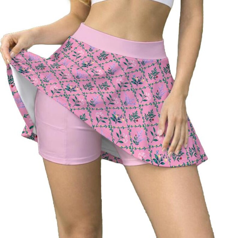 Peut inclure: Une jupe-short de sport rose avec une taille haute et un pan de jupe &eacute;vas&eacute; orn&eacute; d'un motif en treillis r&eacute;p&eacute;titif de vignes vertes, de petites fleurs bleues et de fleurs roses. Le v&ecirc;tement comprend un short int&eacute;gr&eacute; rose clair uni.