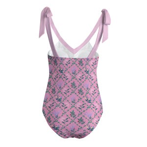 Peut inclure: Un maillot de bain une pi&egrave;ce avec une base rose orn&eacute;e d'un motif en treillis vert et de petits dessins de fleurs et de feuilles. Le v&ecirc;tement pr&eacute;sente des bretelles rose clair qui se nouent sur le dessus et une doublure blanche &agrave; l'encolure.