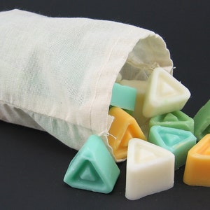 May include: A white cotton drawstring bag spilling out triangular shaped wax melts in various colours, including green, white, and orange.