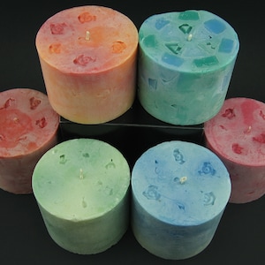 Puede incluir: Seis velas pilares en varios colores, incluyendo rojo, naranja, verde y azul. Cada vela tiene un diseño único en la parte superior, algunas con un patrón floral y otras con formas geométricas.