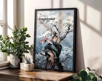 May include: Black framed art print featuring the word "Vagabond" with a samurai warrior illustration. The artwork depicts a figure with swords, set against a backdrop of white flowering trees and a blue sky. The print is displayed on a wooden surface.