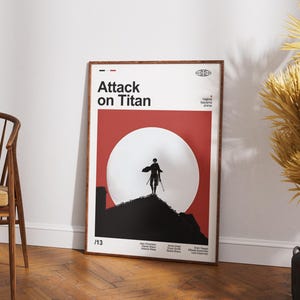 Puede incluir: Póster enmarcado con el título "Attack on Titan" en blanco sobre un fondo rojo y blanco. La obra de arte representa una figura silueteada con espadas de pie sobre una colina negra contra un gran círculo blanco. El póster está en un marco de madera.