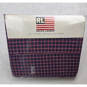 Peut inclure: Un drap plat emballé de Ralph Lauren. Le drap est bleu marine avec un motif à carreaux rouges. L'emballage comprend le logo Ralph Lauren et le texte "100% Coton One Full Flat Sheet."