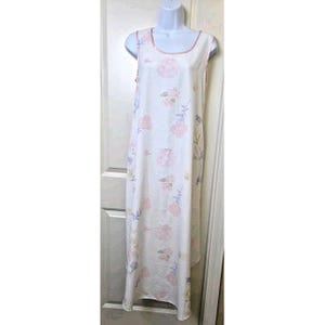May include: A sleeveless, floor-length white dress with a floral pattern. The dress features pink and purple flowers with green leaves. The neckline and armholes are trimmed with a pink ribbon. The dress is displayed on a white mannequin.