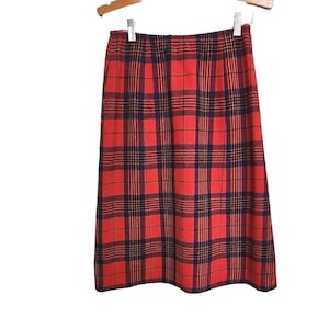 May include: A red plaid skirt with a navy and gold grid pattern, hanging on a wooden hanger. The skirt is knee-length and made of a woven fabric. The plaid pattern is a classic design.