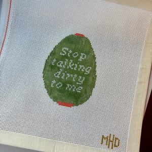 May include: Needlepoint canvas with a green oval design that reads "Stop talking dirty to me" in white text. The canvas has a white mesh background, a beige border, and the initials "MHD" in the bottom right corner.