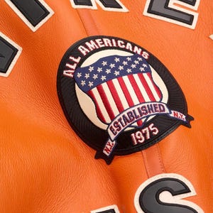 ack view of a handmade men's vibrant orange leather B3 bomber jacket featuring large black and white AVIREX USA varsity lettering