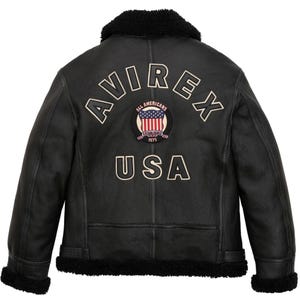 May include: Black leather jacket with a shearling collar and trim. The back features the word "AVIREX" in white lettering, along with a circular patch displaying the American flag and the text "ALL AMERICANS ESTABLISHED 1975 USA".