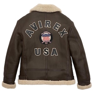 Back view of a handmade dark brown leather B3 bomber jacket showing large beige and black AVIREX USA varsity lettering and a central American flag shield patch.
