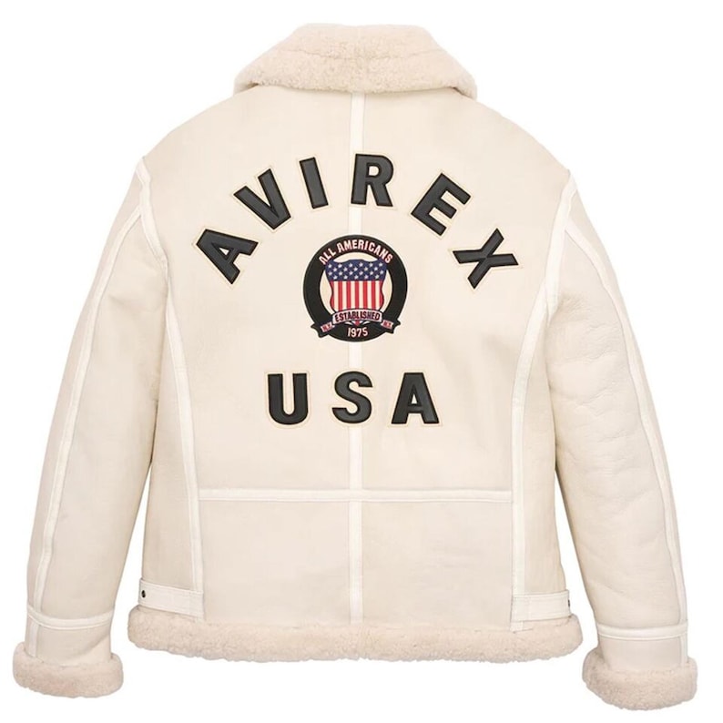 May include: Cream-colored shearling jacket with a sheepskin collar and cuffs. The back features the word "AVIREX" above a circular emblem with the words "All Americans" and "USA" below. The emblem includes a red, white, and blue design.