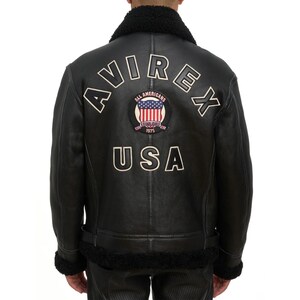 May include: Black leather jacket with a shearling collar and lining. The back features the word "AVIREX" in white lettering, along with a patch that says "ALL AMERICANS ESTABLISHED 1975 USA".