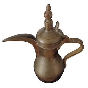 Pode incluir: Uma cafeteira de latão vintage com um bico longo, uma alça curva e um botão decorativo na tampa. A cafeteira tem um corpo bulboso e é provavelmente usada para servir café ou chá. O latão tem uma pátina quente e envelhecida.