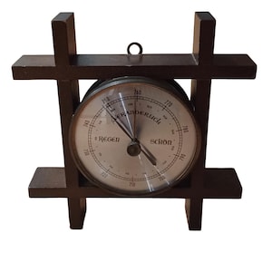 May include: A vintage barometer with a circular gauge, set within a dark brown wooden frame. The gauge features a silver face with black numerals and the words "Regen" and "Schon". A small metal loop is at the top for hanging.