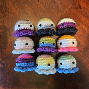 May include: Nine small, round, crocheted octopus figures arranged in a three-by-three grid. Each figure features horizontal stripes in various colour combinations, a ruffled base, and two small, black, circular plastic eyes on the front.