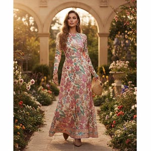 May include: A long-sleeved floral print maxi dress in cream, pink, and blue tones. The dress features a high neckline and a flowing skirt. A woven straw handbag is held in the hand. The background includes a garden setting with stone arches and blooming flowers.