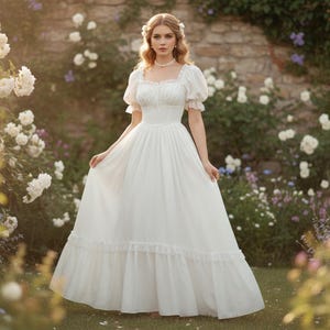 May include: A white, floor-length dress with a square neckline and short, puffed sleeves. The dress features a fitted bodice and a flowing skirt with a ruffled hem. The background includes white roses and a stone wall.
